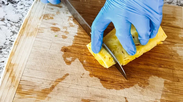 Wearing blue disposable gloves for hygiene, someone is skillfully slicing into a juicy organic watermelon on a wooden cutting board, set on a clean kitchen countertop.