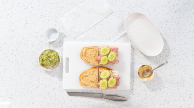 Düz yatıyordu. Beyaz kesme tahtasının üzerinde jambon, salatalık ve filizli sandviçler birleştirmek..