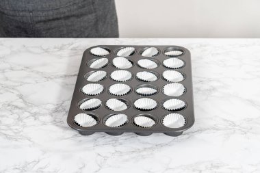 Scooping cupcake batter with dough scoop into a baking pan with liners to bake American flag mini cupcakes.