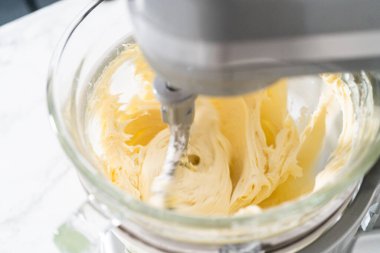 Whisking buttercream frosting in a glass mixing bowl with an electric kitchen mixer for American flag mini cupcakes.