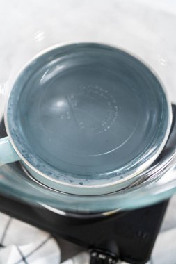 Eriyen beyaz çikolata parçaları ve diğer malzemeler kaynamış suyun üzerine karıştırıp çubuk şekerleme hazırlıyor..