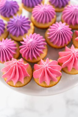 Beyaz pasta standında pembe tereyağlı taze pişmiş mini vanilyalı kekler..