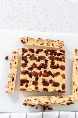 Beyaz çikolatalı fındıklı fındıklı şekerlemeyi beyaz bir kesme tahtasında küçük parçalara ayırmak..