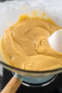 Eriyen beyaz çikolata parçacıkları ve diğer malzemeler kaynamış suyun üzerinde karışıp kızılcık fıstıklı şekerleme hazırlıyor..