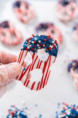 Dipping pretzels twists into melted chocolate to make red, white, and blue chocolate-covered pretzel twists.