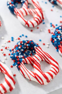 Dipping pretzels twists into melted chocolate to make red, white, and blue chocolate-covered pretzel twists.