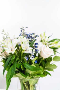 Taze beyaz güllerin ve çeşitli çiçeklerin bulunduğu büyüleyici bir buket, zarif bir vazoda düzenlenmiş, zamansız bir güzellik yayıyor..