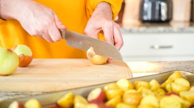 Modern bir mutfağın hoş geldin ortamında genç bir adam akşam yemeği hazırlama sürecine devam ediyor. Şu anda sarı soğanları halka şeklinde dilimleyip ızgara yapmaya hazırlanıyor.