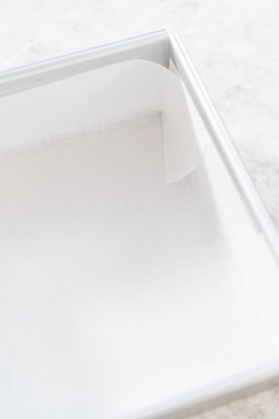 Çubuk şekerleme hazırlamak için kare peynirli kek tepsisini parşömen kağıdıyla kaplamak.