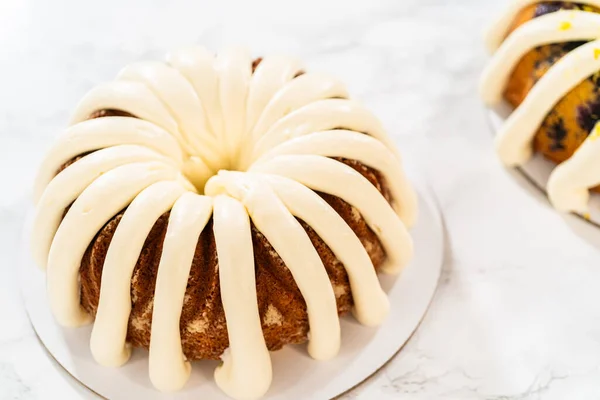 The final stage of this delightful baking journey involves artistically piping the silky cream cheese buttercream frosting atop the cooled bundt cakes, creating an irresistible treat.