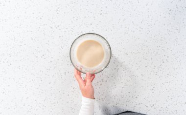 Flat lay. Mixing ingredients with a hand whisk in a glass mixing bowl to make the vanilla glaze.