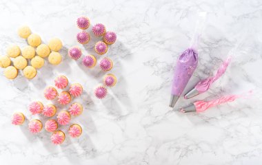 Düz yatıyordu. Mini vanilyalı keklerin üzerine pembe tereyağlı krema sıkıyorum..