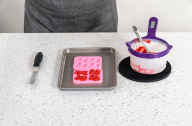 Flat lay. Filling bow silicone chocolate mold with melted chocolate to make a chocolate pretzel Christmas wreath.