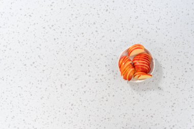 Düz yatıyordu. İnce dilimlenmiş kırmızı elmalar beyaz bir tabakta.