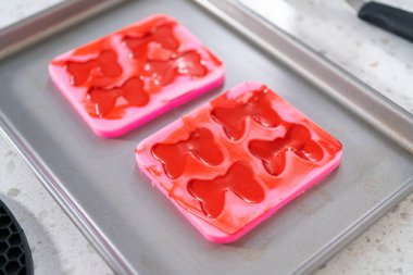 Flat lay. Filling bow silicone chocolate mold with melted chocolate to make a chocolate pretzel Christmas wreath.