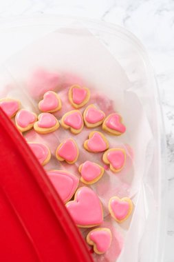 Kalp şeklinde şeker kurabiyelerini büyük plastik bir kapta pembe ve beyaz kraliyet kreması ile depolamak.