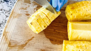 Hijyen için mavi tek kullanımlık eldivenler giyen biri, temiz mutfak tezgahına kurulmuş, ahşap kesme tahtasındaki sulu organik karpuzu ustalıkla dilimliyor..