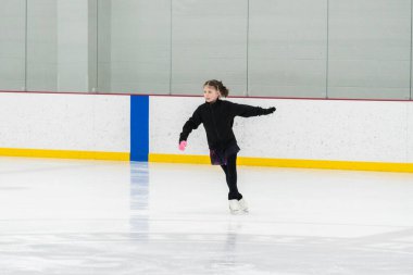 Artistik patinaj rutinini mükemmelleştiren genç bir kız kapalı bir buz pateni sahasında yarışma elbisesini giyerken.