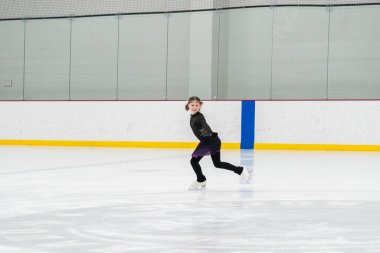 Artistik patinaj rutinini mükemmelleştiren genç bir kız kapalı bir buz pateni sahasında yarışma elbisesini giyerken.