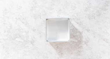 Flat lay. Lining square cheesecake pan with parchment paper sheet to prepare chocolate hazelnut fudge.