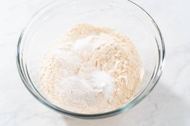 Beyaz çikolatalı macadamia fındığı pişirmek için bardakta çırpma kabıyla kurutulmuş malzemeleri karıştırıyorum..