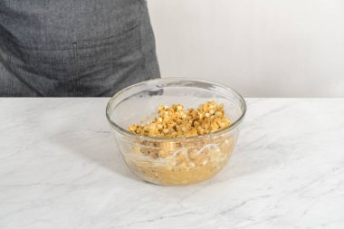 Islak ve kuru malzemelerle karıştırılmış cam bir kabın içinde çırpılmış beyaz çikolatalı makadamia fındığı..