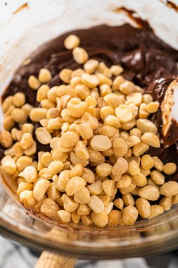 Beyaz çikolata parçacıkları ve diğer malzemeleri kaynayan suyun üzerine karıştırıp çikolatalı macadamia şekerlemesi hazırlıyorum..