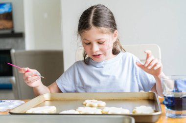 Küçük bir kızın özenle yazdığı iç açıcı bir sahne. Şekerli kurabiyelerin üzerine besin boyası sürmüş. Kurabiyeler güzel bir şekilde beyaz kraliyet kreması ile dolmuş..