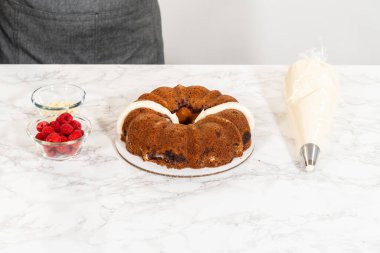 Hassasiyetle, Beyaz Çikolatalı Ahudududulu Çörek dikkatlice tavadan çıkartılır. Lezzetli krem peynirli kremayla süslenir ve lezzetli bir ziyafet yaratır..