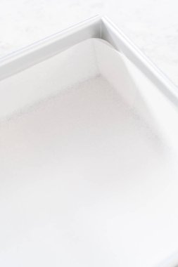 Kızılcık fıstıklı şekerleme hazırlamak için kare peynirli kek tavasını parşömen kağıdıyla kaplamak.