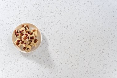 Düz yatıyordu. Beyaz seramik tabakta ev yapımı beyaz çikolatalı fındıklı şekerleme parçaları..