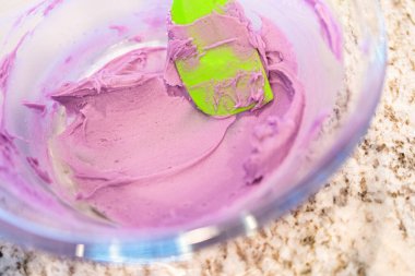 İyi ışıklandırılmış bir mutfakta, yeşil ve diğer renklerin çeşitli tonlarında tereyağlı krema çeşitleri büyüleyici kapkeklerin sanatsal dekorasyonu için titizlikle karıştırılıyor ve hazırlanıyor.