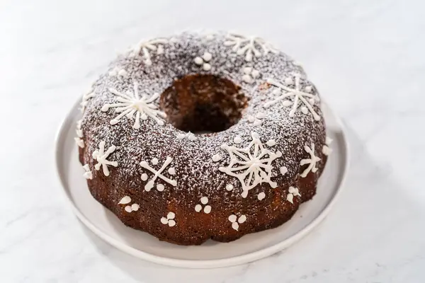 Gingerbread bundt cake with caramel filling, buttercream frosting, and powdered sugar dusting on the kitchen counter.