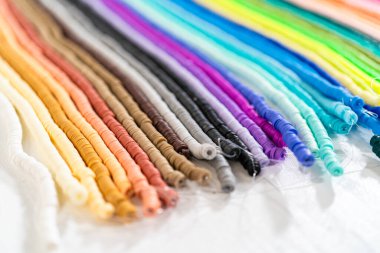 Beyaz bir masadaki renklere göre düzenlenmiş canlı bir kil boncuk koleksiyonu genç zanaatkarlara kendi eşsiz bileziklerini yapmaları için ilham vermeye hazır..