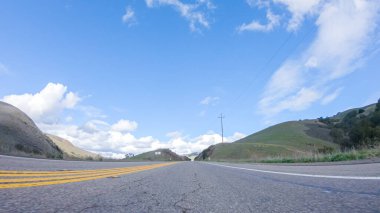 Araç, parlak güneşin altında Cuyama Otoyolu boyunca ilerliyor. Çevresindeki manzara, ışık saçan güneş ışığıyla aydınlanır ve araba seyahat ederken güzel ve davetkar bir sahne yaratır.