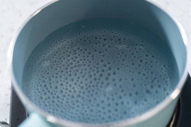 Çikolata parçacıkları ve diğer malzemeleri kaynayan suyun üzerinde karıştırarak çikolatalı şekerleme ve fıstık ezmesi karışımı hazırlıyorum..