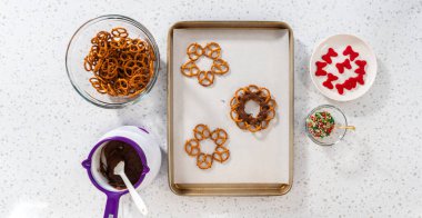 Flat lay. Dipping pretzels twists into melted chocolate to make a chocolate pretzel Christmas wreath.