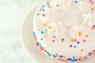 Beyaz kek tabağına funfetti serpiştirilmiş küçük beyaz doğum günü pastası.