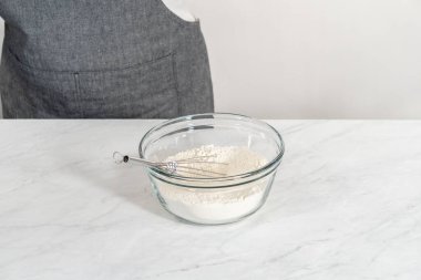Beyaz çikolatalı macadamia fındığı pişirmek için bardakta çırpma kabıyla kurutulmuş malzemeleri karıştırıyorum..
