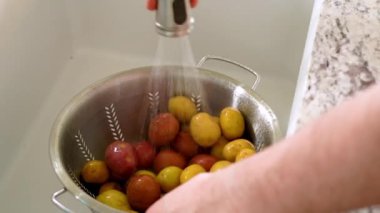 Parlak, modern mutfakta, genç bir adamın akşam yemeği için özenle hazırlandığı görülüyor. Şimdiki görevi lavaboda küçük gökkuşağı patateslerini yıkamak.