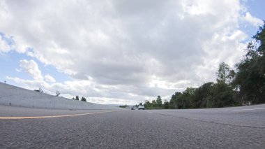 Bulutlu bir kış gününde, bir araba, Santa Maria, California yakınlarındaki 101. Otoyol boyunca bulutlu bir gökyüzünün altında, yeşil ve altın renkli bir karışımla sorunsuzca yol alır..