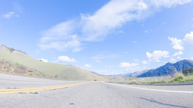 Araç, parlak güneşin altında Cuyama Otoyolu boyunca ilerliyor. Çevresindeki manzara, ışık saçan güneş ışığıyla aydınlanır ve araba seyahat ederken güzel ve davetkar bir sahne yaratır.