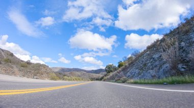 Araç, parlak güneşin altında Cuyama Otoyolu boyunca ilerliyor. Çevresindeki manzara, ışık saçan güneş ışığıyla aydınlanır ve araba seyahat ederken güzel ve davetkar bir sahne yaratır.