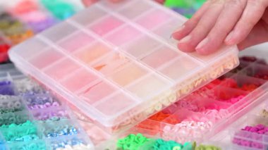 Parlak renkli balçık boncuklarından oluşan geniş bir koleksiyonu bölümlere ayıran eller, karmaşık malzemelerin güzelliğini ve çeşitliliğini vurguluyor.