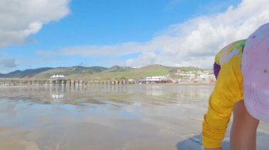 Küçük bir kız kışın soğuğu için Pismo Sahili 'nde kışın deniz kabuğu ve istiridye ararken sevinçle istiridye topluyor..