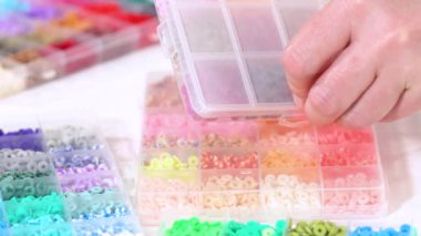 Parlak renkli balçık boncuklarından oluşan geniş bir koleksiyonu bölümlere ayıran eller, karmaşık malzemelerin güzelliğini ve çeşitliliğini vurguluyor.