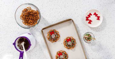 Flat lay. Dipping pretzels twists into melted chocolate to make a chocolate pretzel Christmas wreath.