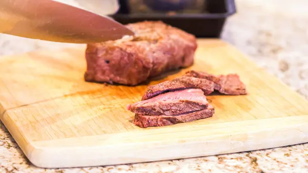 Gloved chef slices succulent pink steak on natural bamboo board, kitchen backdrop.