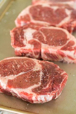 Modern beyaz bir mutfakta, baharatlı bir pirzola bifteği, güzel mermerleriyle övünerek, bir pişirme çarşafının üzerinde oturur. Açık hava gaz ızgarası için hazırlanıyor, mükemmel bir kavurucu söz veriyor.