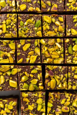 Cutting chocolate pistachio fudge with a large kitchen knife into square pieces on a white cutting board.